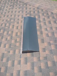 Gray rectangular roof vent on a brown and gray shingle roof.
