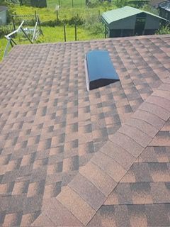 Brown and tan asphalt shingle roof with a skylight. In a rural outdoor setting.