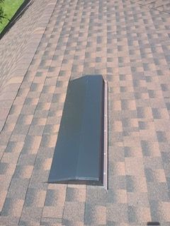 Dark, rectangular roof vent on a brown and tan shingle roof.