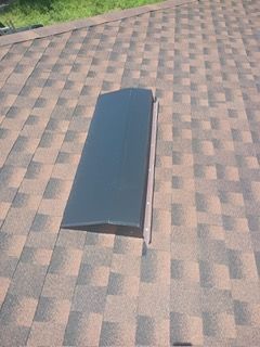 Black vent on a brown and black shingled roof.