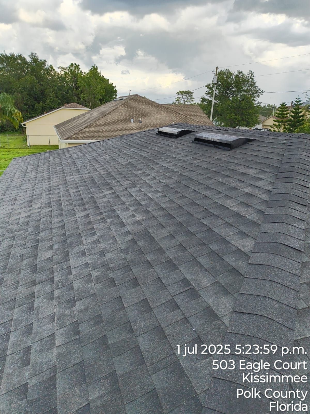 Dark gray shingled roof with two vents, a Kissimmee, Florida address visible, overcast sky.