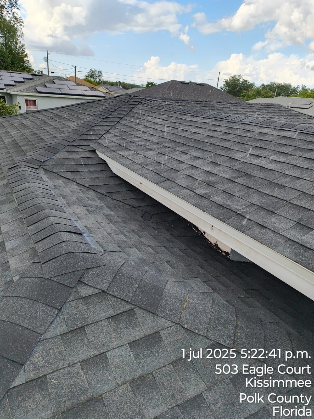 A roof with gray shingles, with a visible damaged area, located in Kissimmee, Florida.
