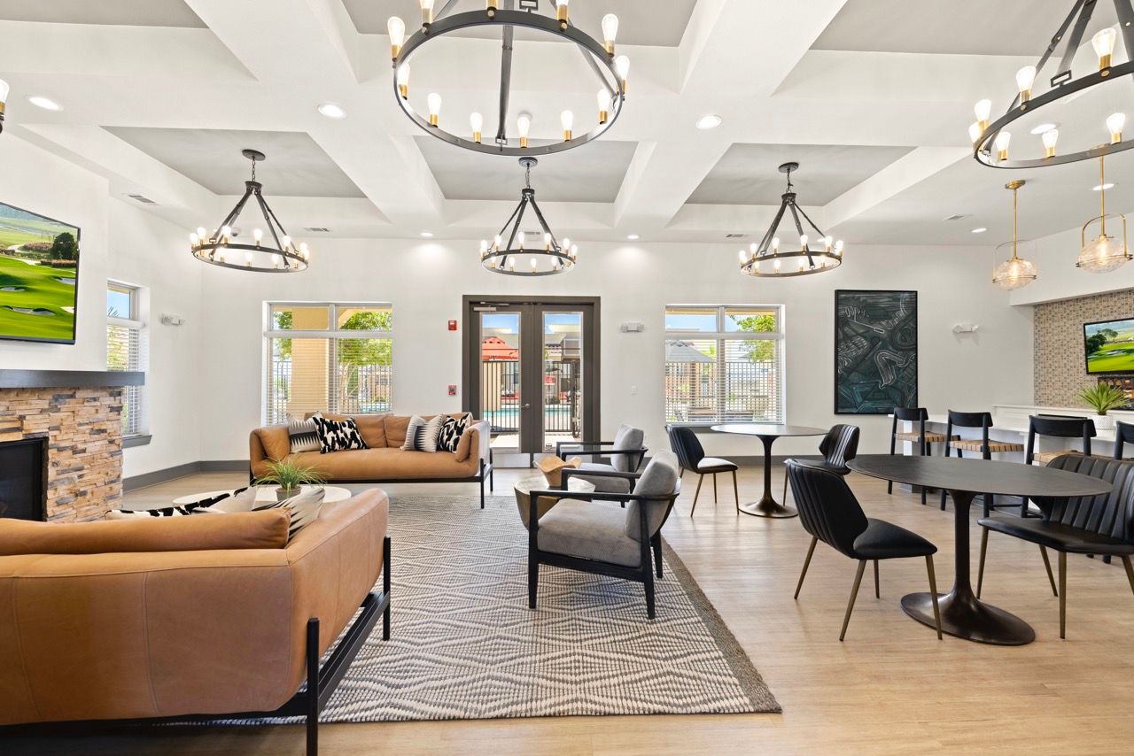 Bright modern resident lounge with tan sofas, armchairs, round tables, and chandeliers.