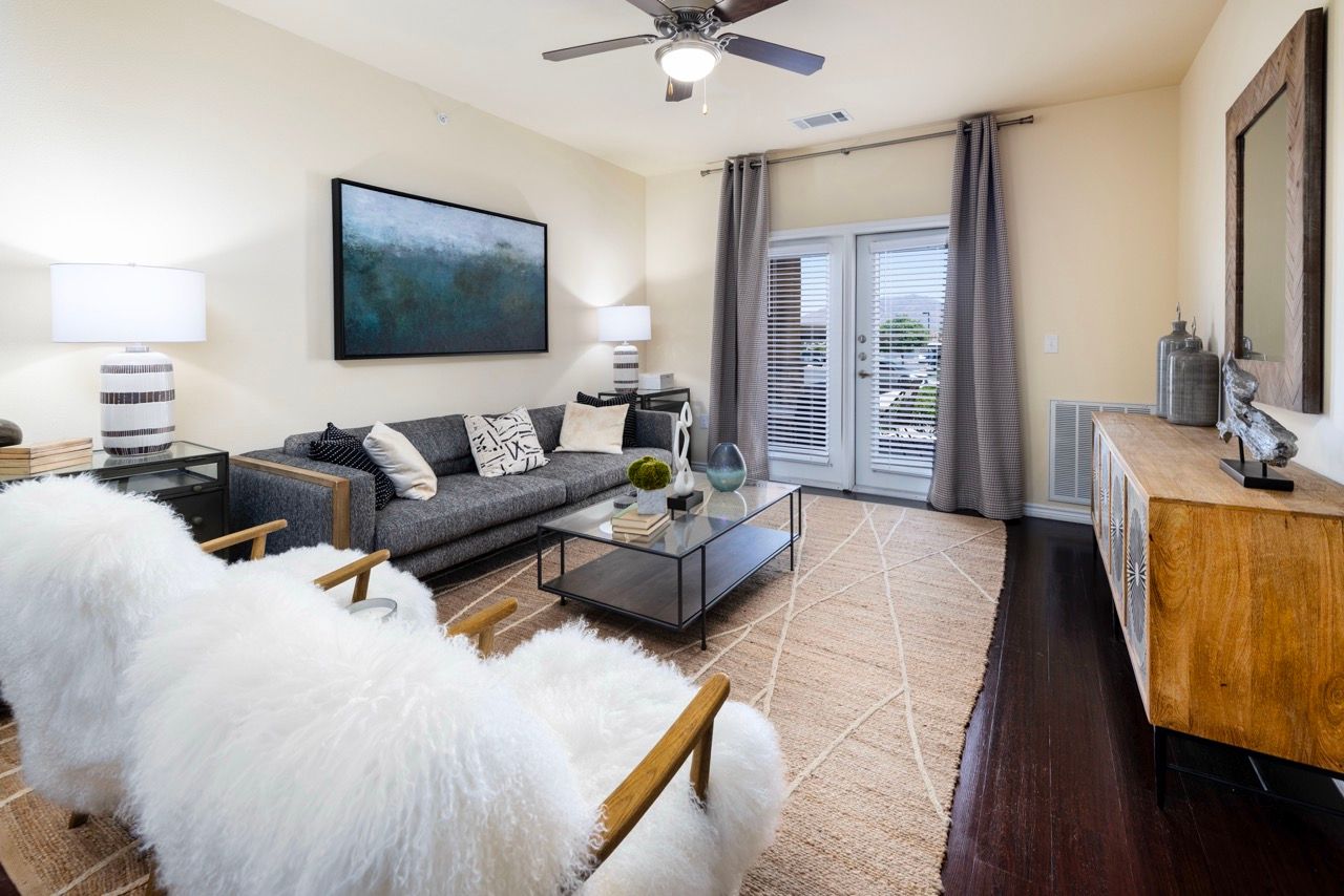 Modern living room with gray sofa, glass coffee table, beige walls, and French doors with gray curtains.