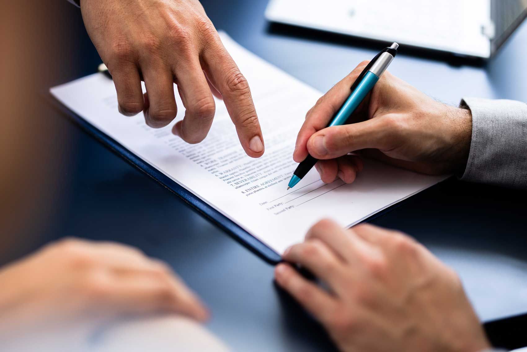 To personer underskriver et dokument ved et skrivebord med et rødt stempel ved siden af.