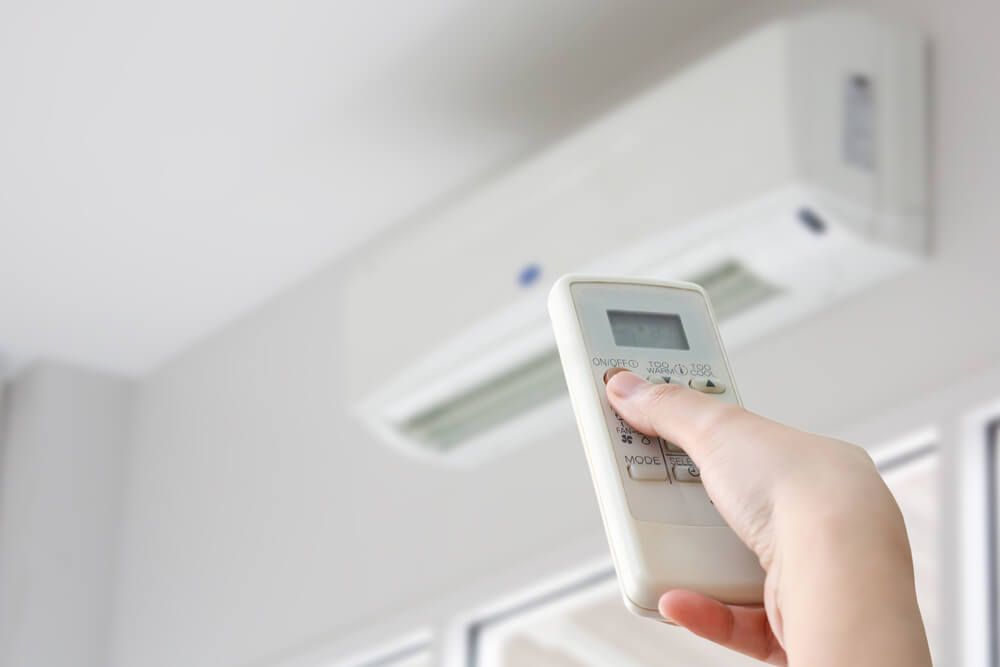 A person is holding a remote control in front of an air conditioner — Gleeson's Air Conditioning in Laurieton, NSW
