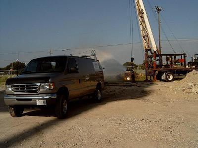 A brown van next to a drilling rig on a gravel road