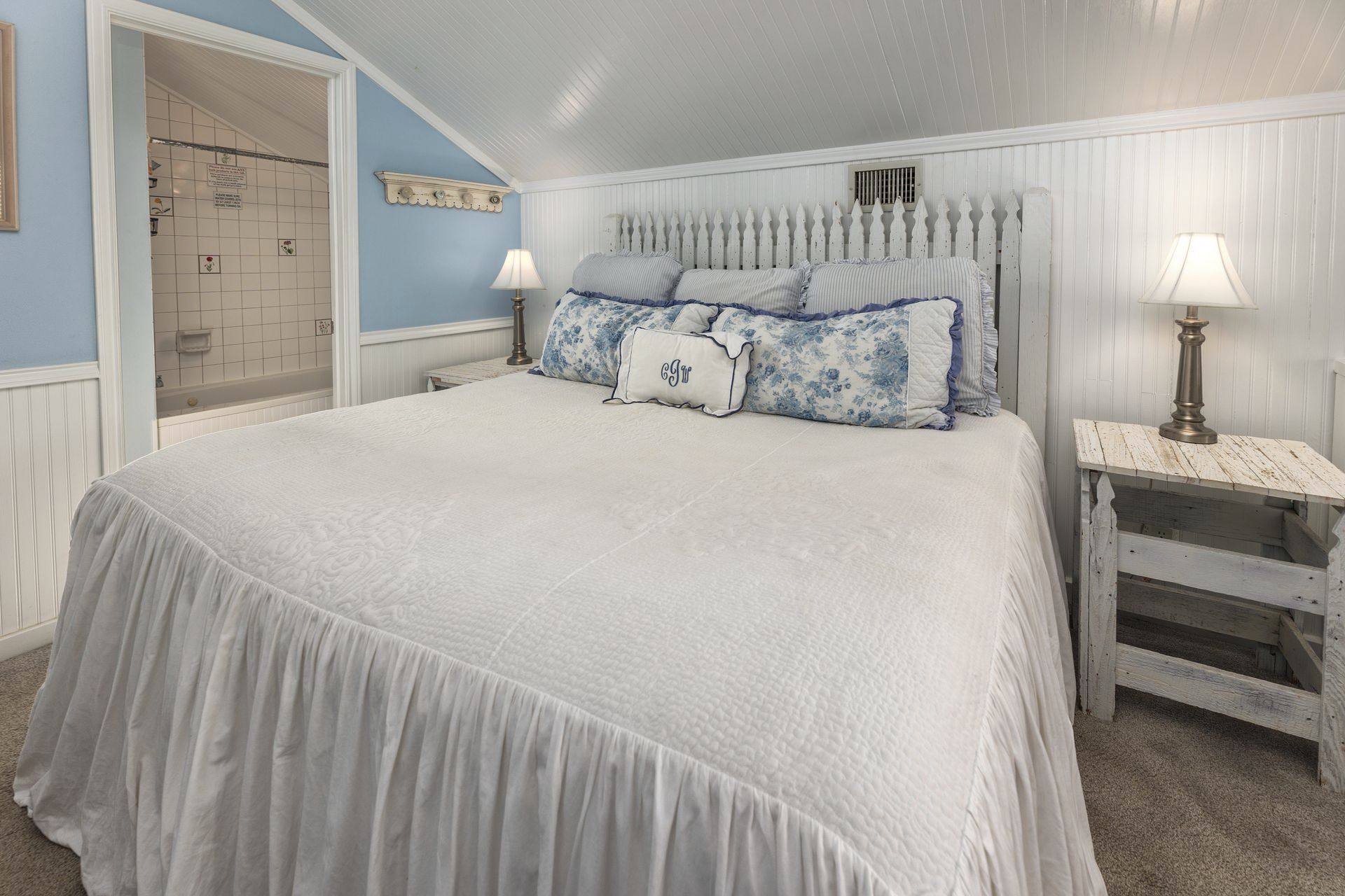 A bedroom with a bed , nightstand , lamps and a bathroom.