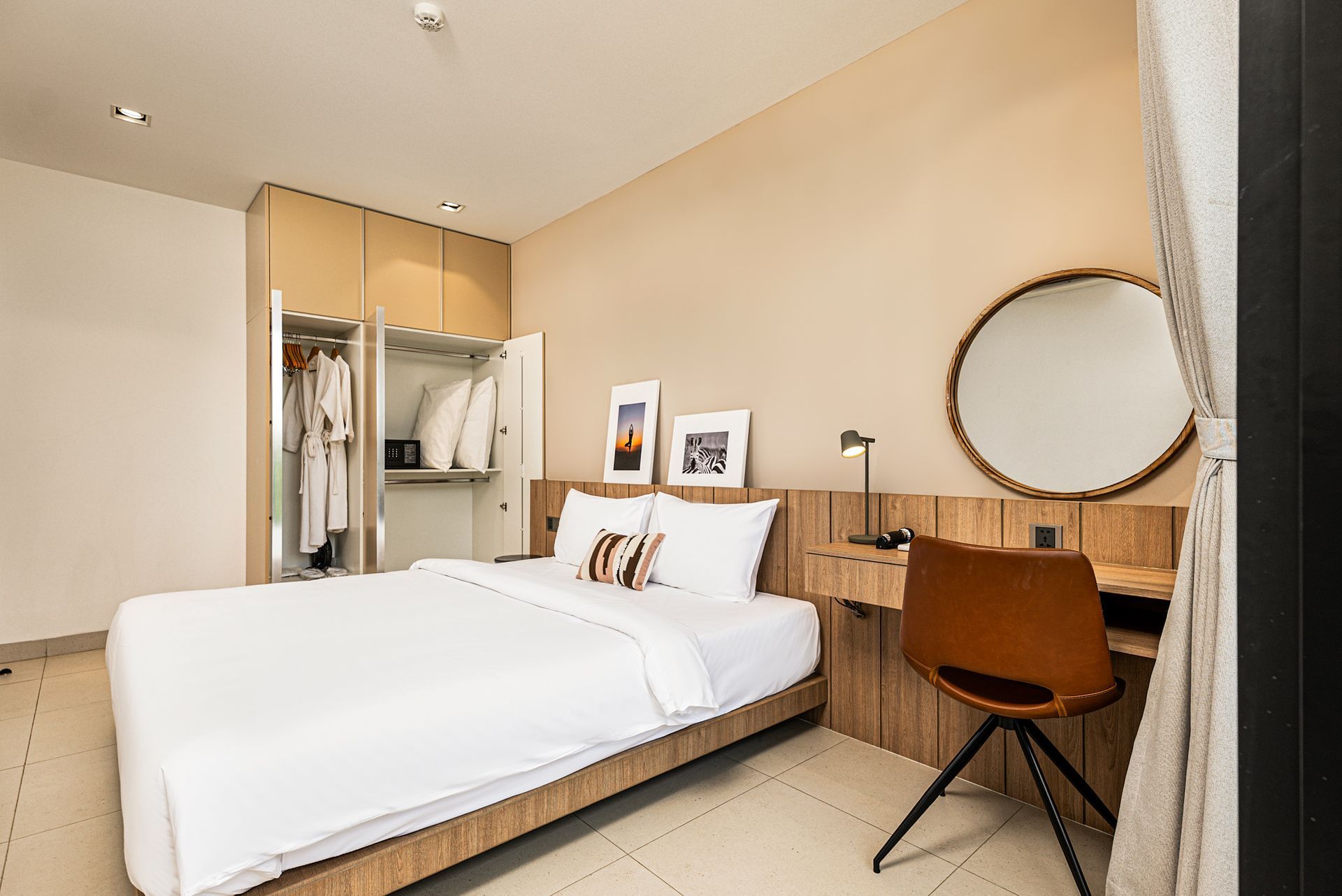 Cozy bedroom with white bed, wooden desk, round mirror, and a chair in a soft beige interior