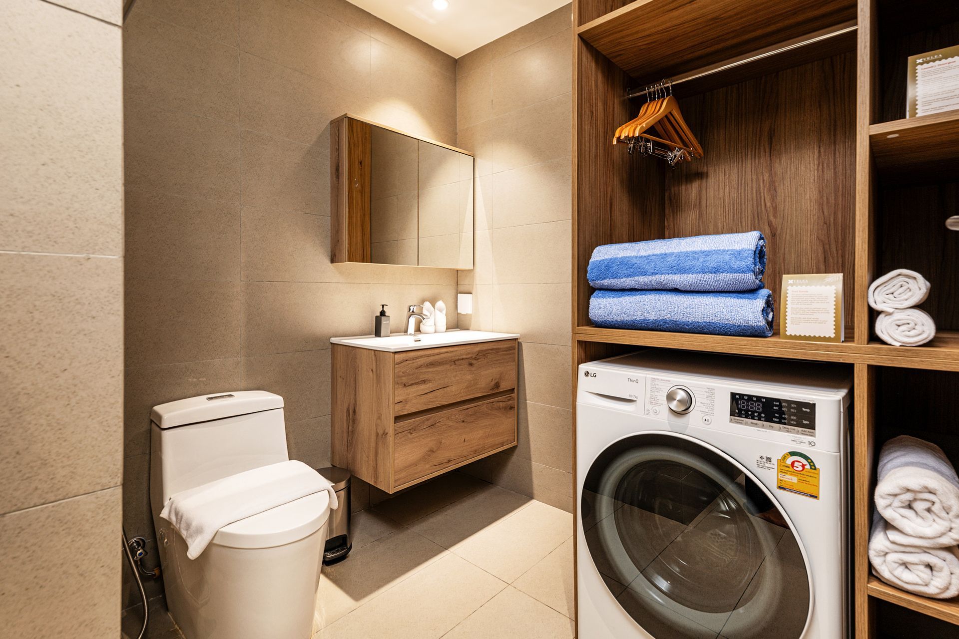 Small bathroom with toilet, wood vanity, and stacked washer-dryer with folded towels.