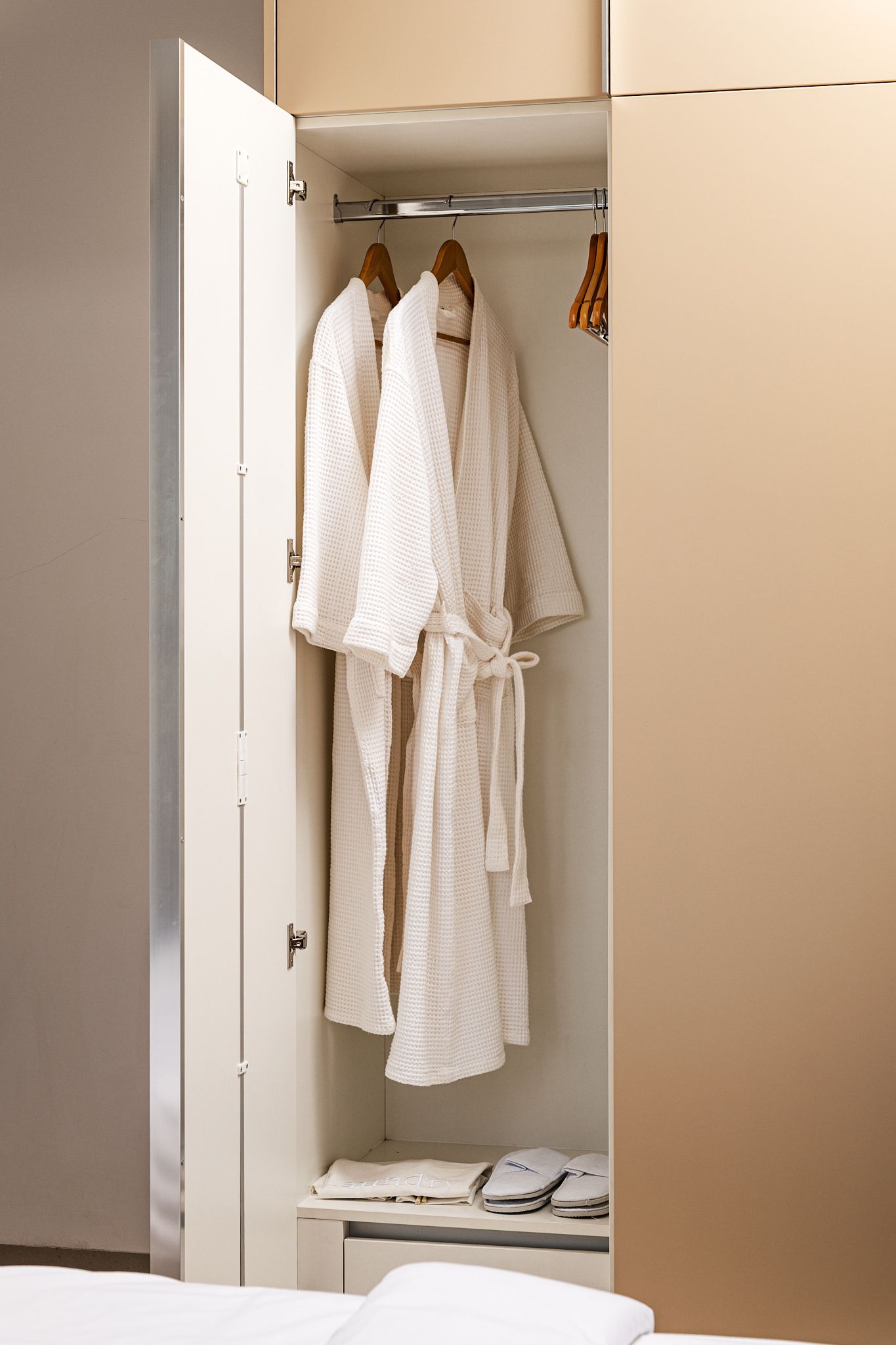 Open wardrobe with white robes hanging inside and a shelf below