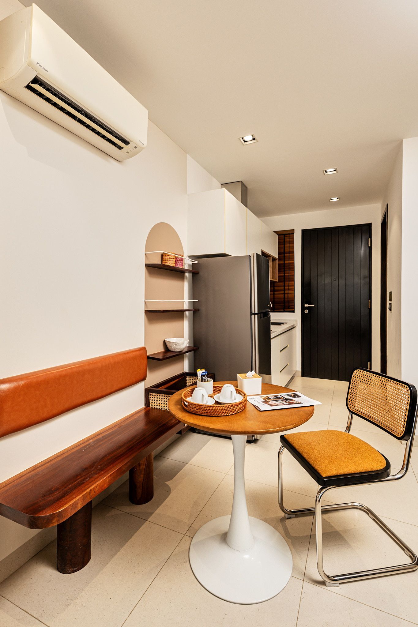 Small café seating area with wooden bench, round table, metal chair, and air conditioner on white walls.