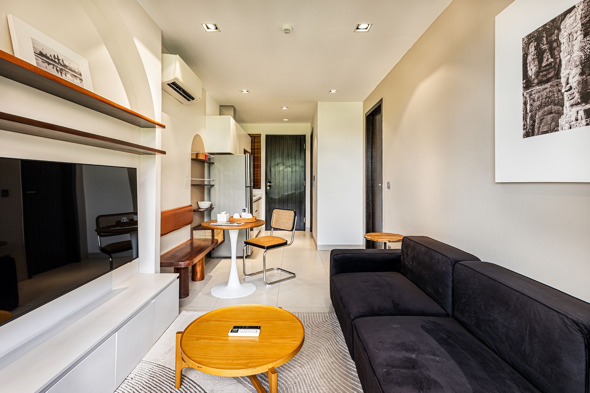 Modern living room with black sofa, TV, wood accents, and a bright open hallway