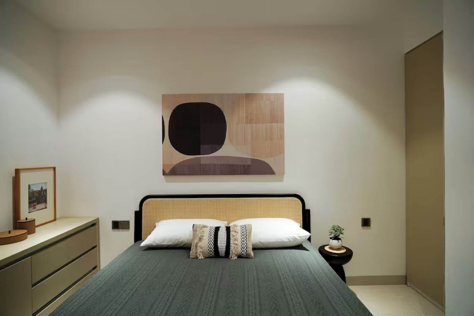 Minimalist bedroom with a bed, dresser, and abstract wall art in soft neutral tones