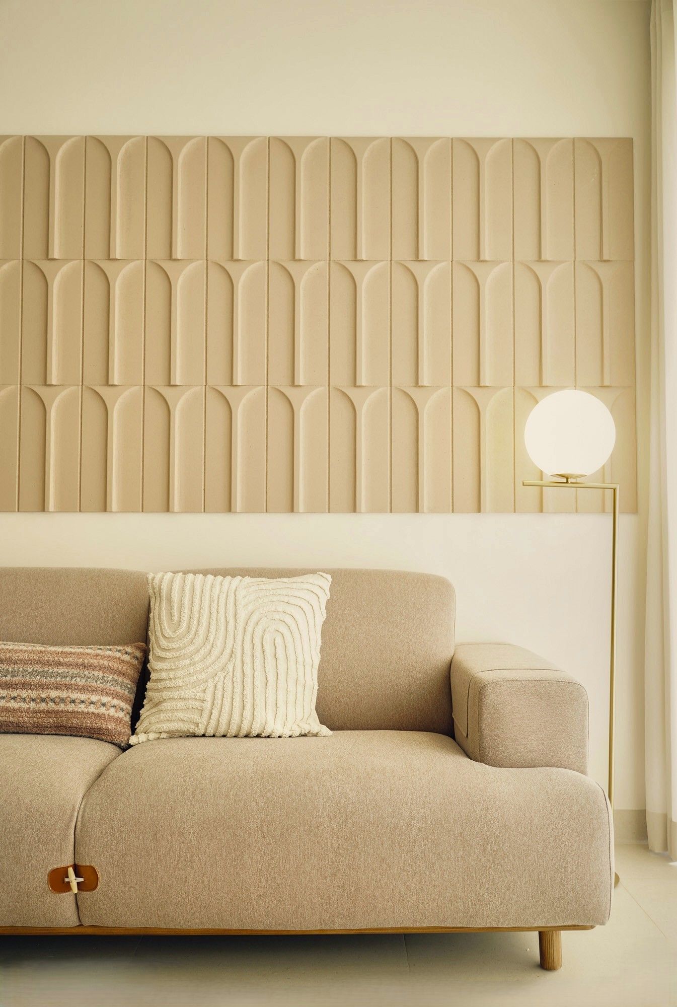 Cozy beige sofa with textured pillows in a warm minimalist living room beside a round lamp