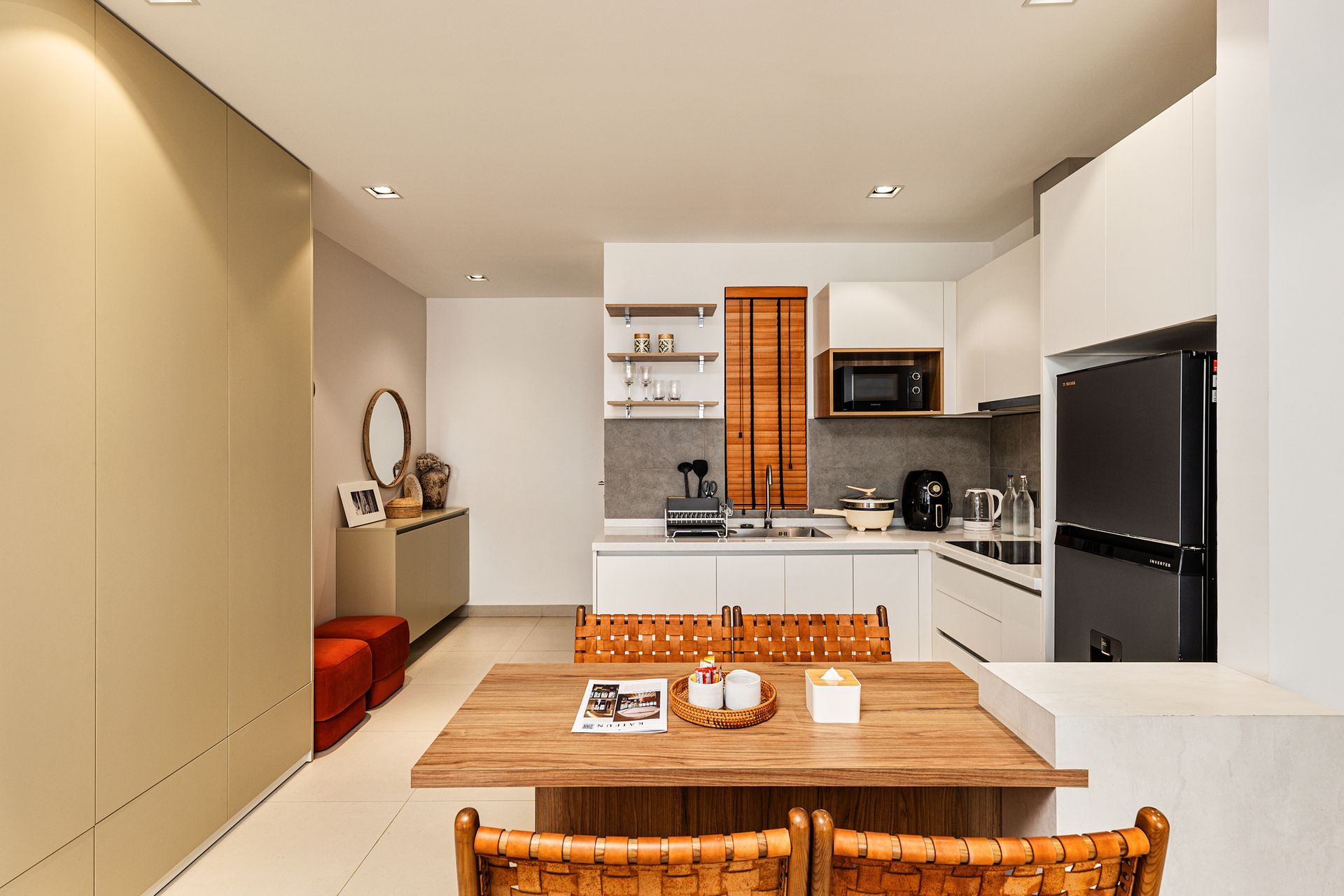 Modern open-plan kitchen and dining area with wooden table, white cabinets, and black refrigerator