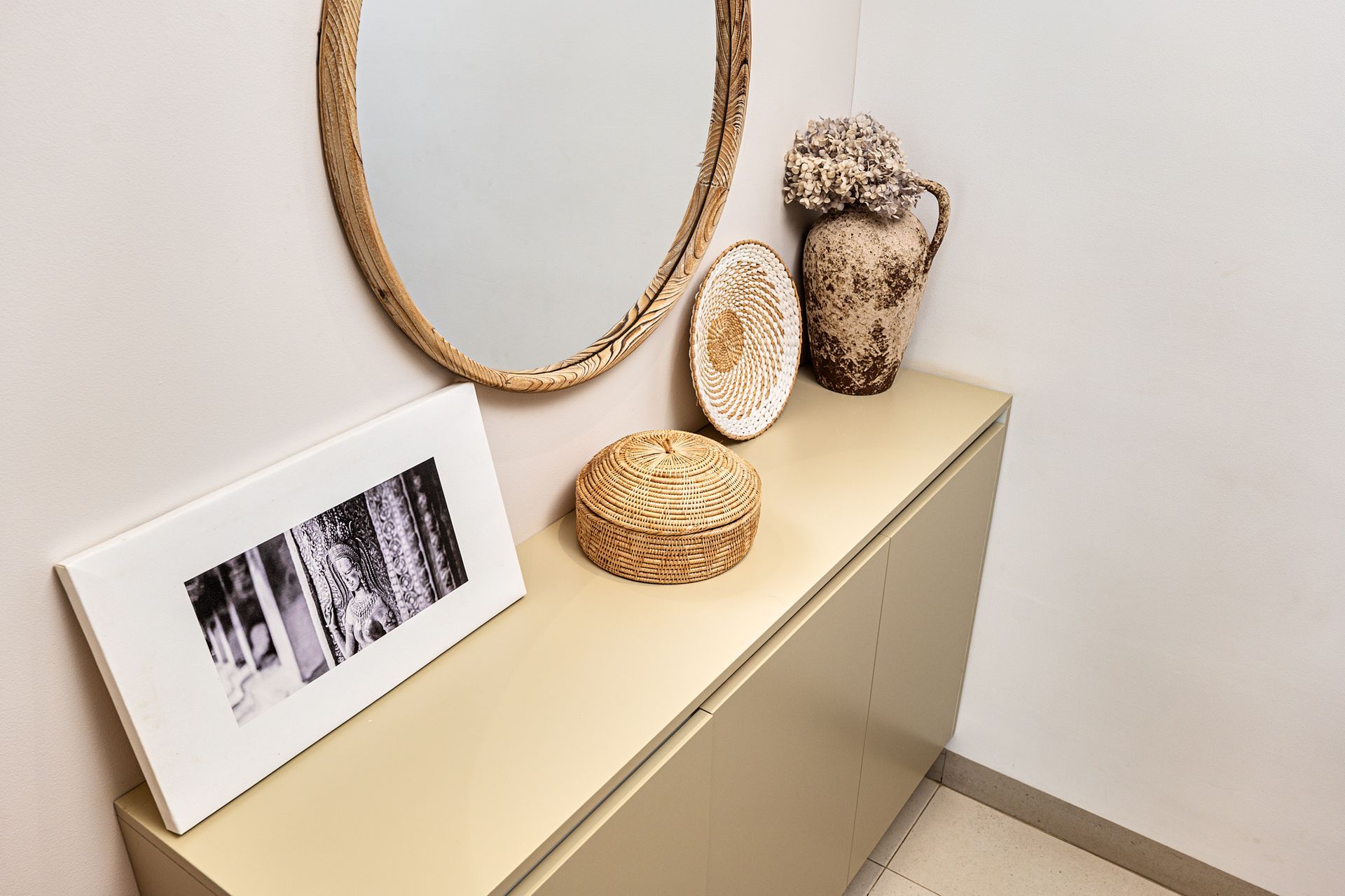 Minimalist beige console table with framed photo, oval mirror, and decorative objects in a bright room