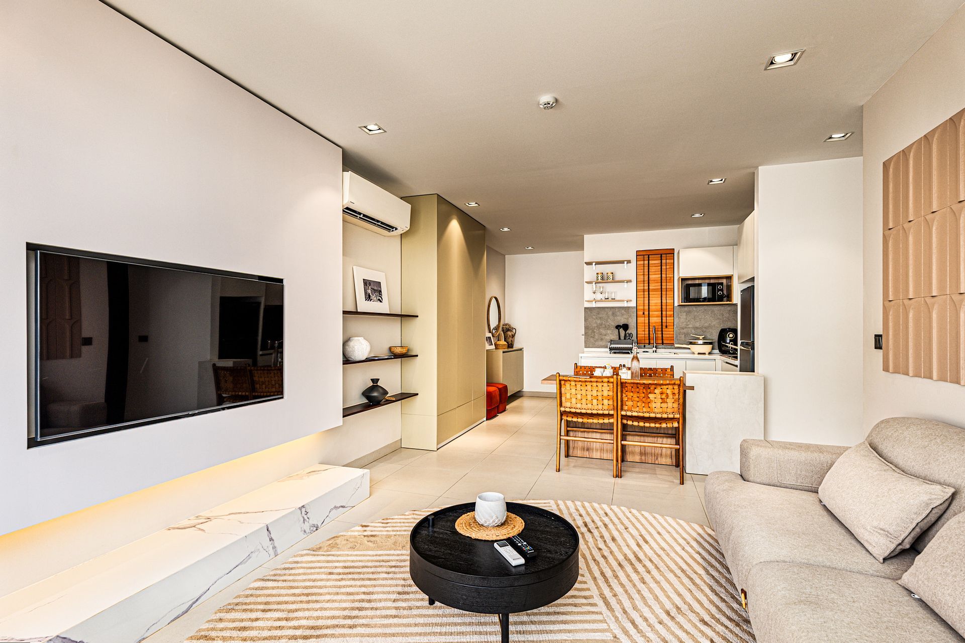 Bright modern living room with beige sofa, round coffee table, woven rug, and kitchen in the background