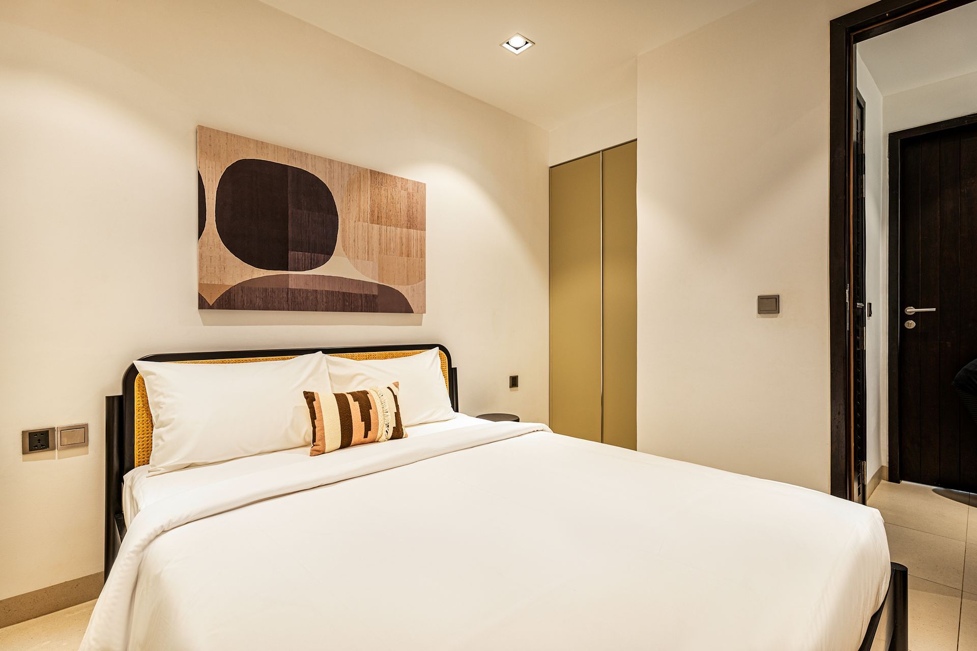 Modern bedroom with a neatly made white bed, abstract wall art, and warm neutral decor