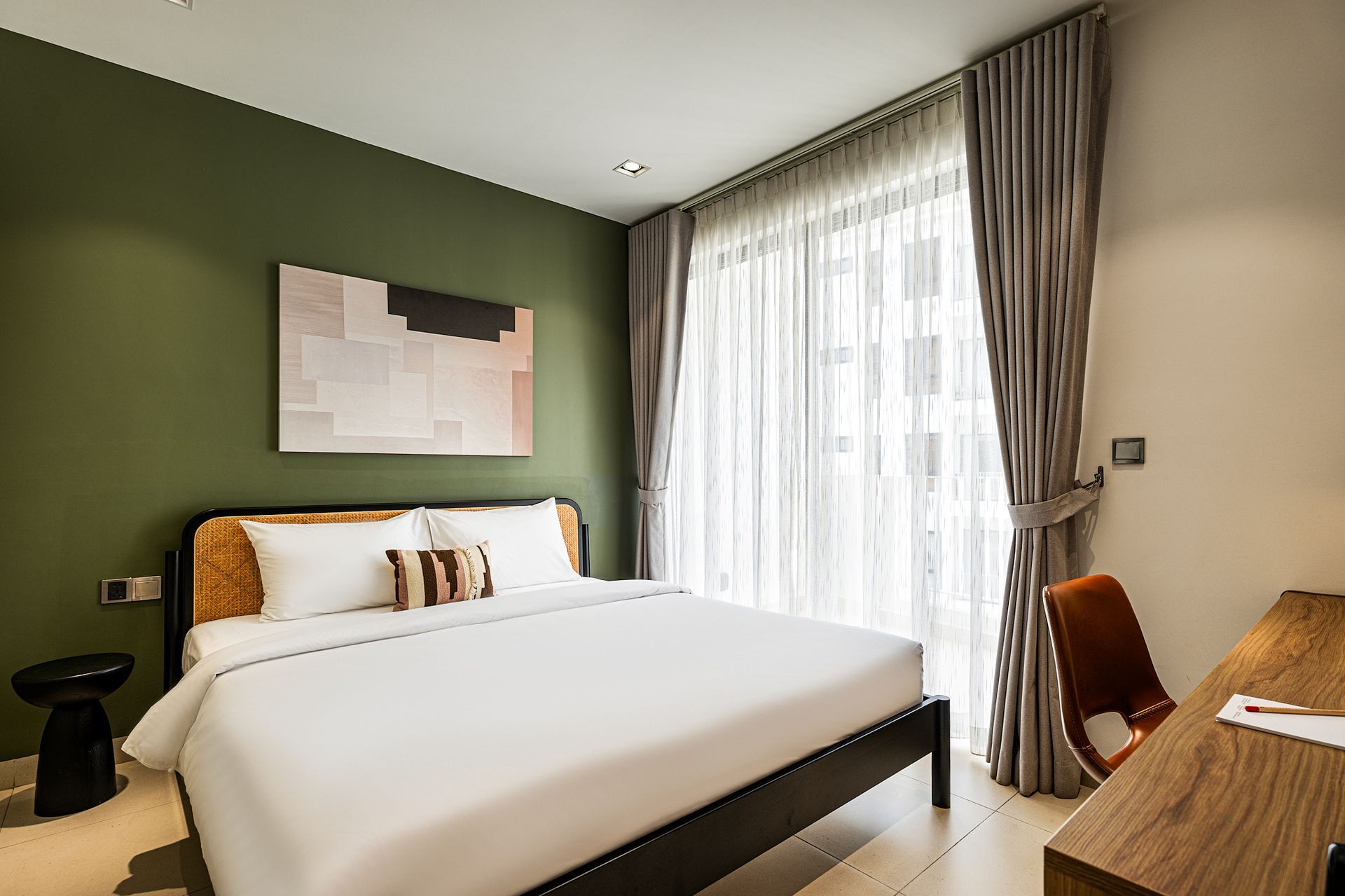 Modern bedroom with a large bed, green accent wall, and floor-to-ceiling window with curtains.
