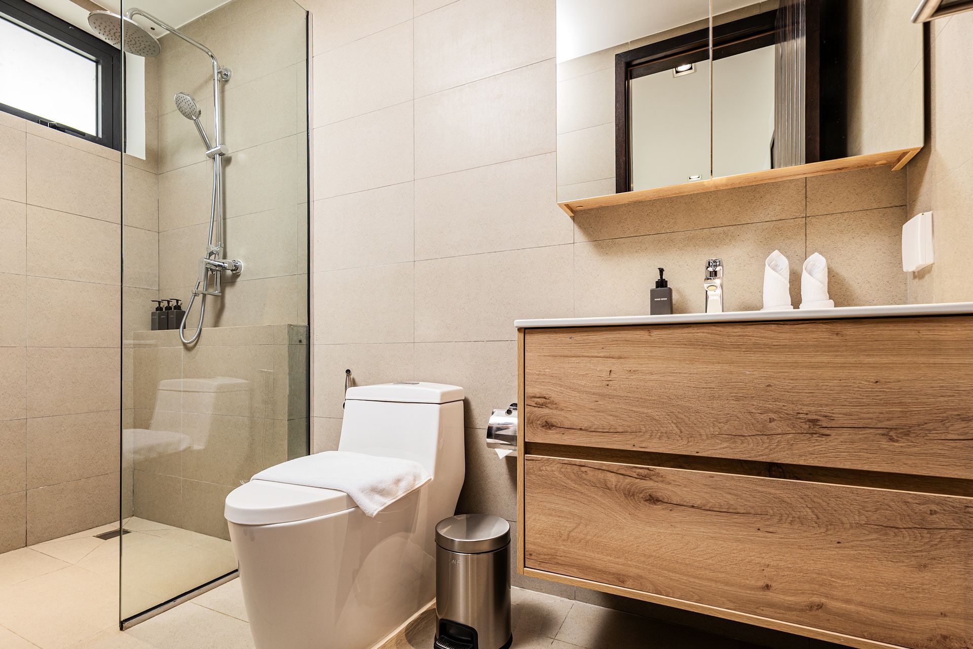 Modern bathroom with toilet, glass shower, wood vanity, and mirror above sink
