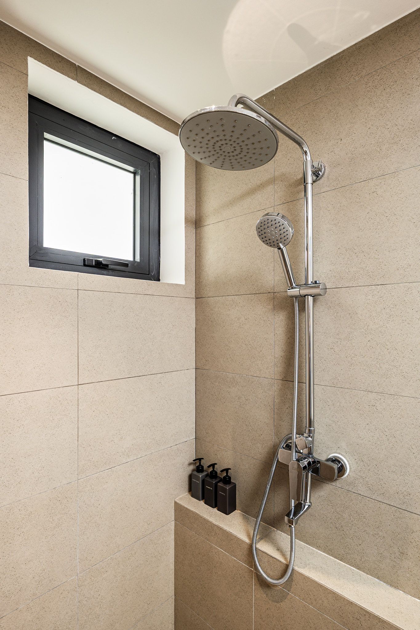 Modern bathroom shower with handheld and rain showerheads, tiled walls, and a small window