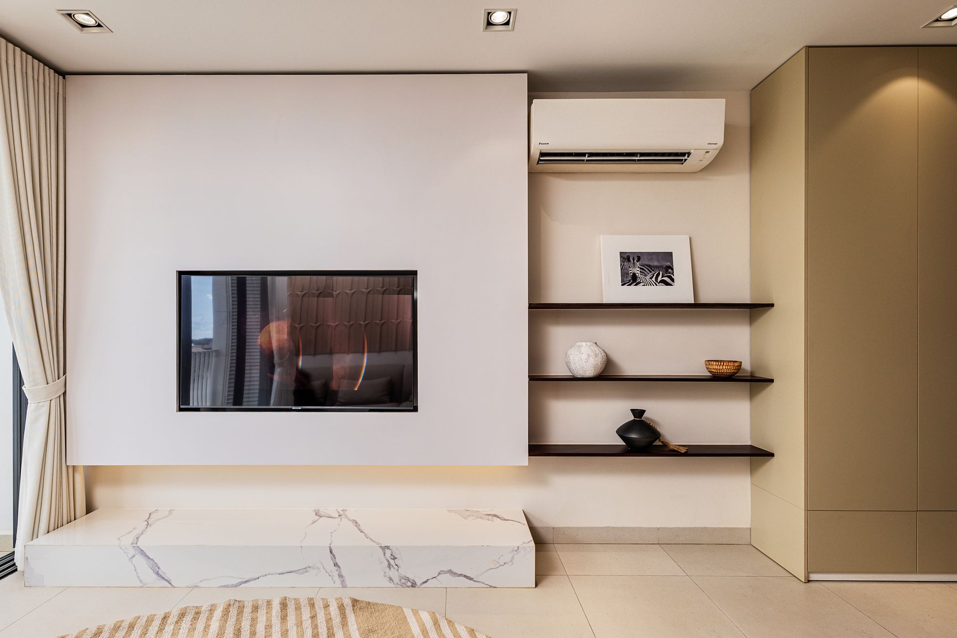 Modern living room with beige sofa, wall-mounted TV, shelves, and large sliding doors to a balcony.