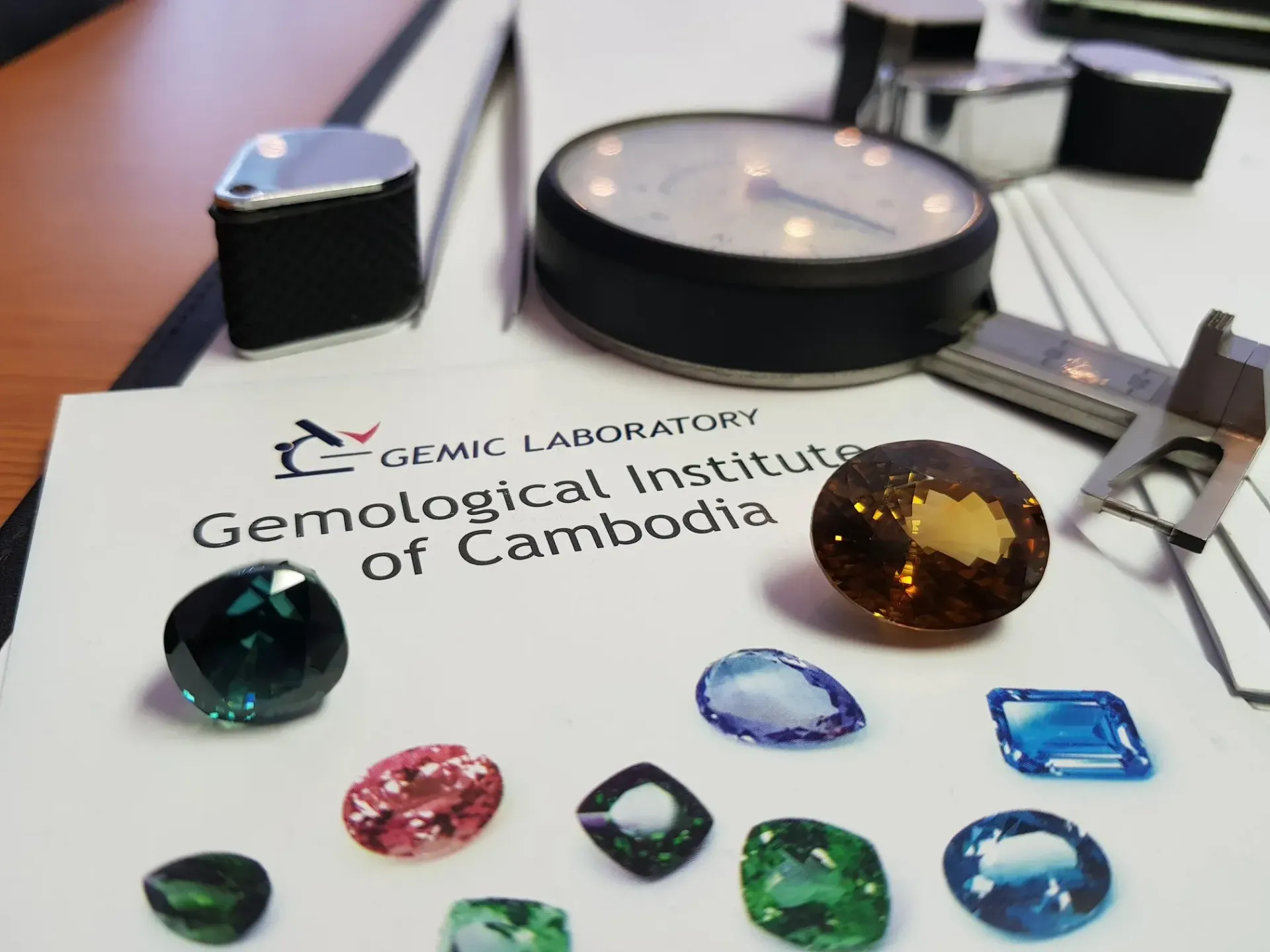 Gemstones on Gemological Institute of Cambodia document with tools.