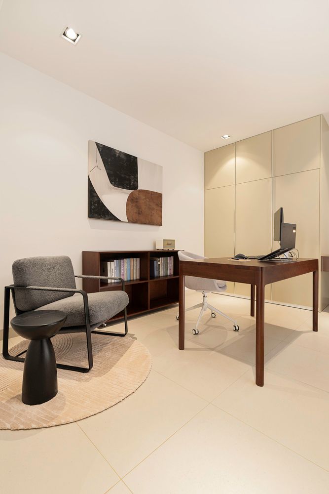Modern office space with desk, chair, bookshelf, artwork, and side table. Neutral colors.