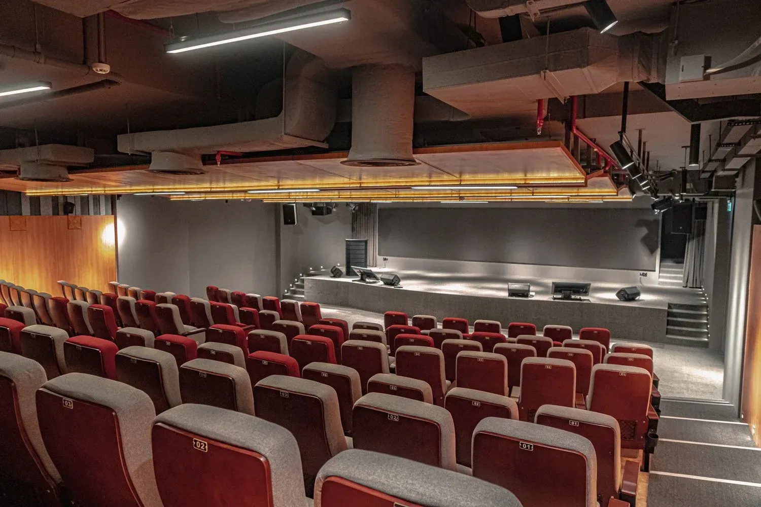 Auditorium with red seats facing a stage; dark walls and ceiling; stage lights visible.