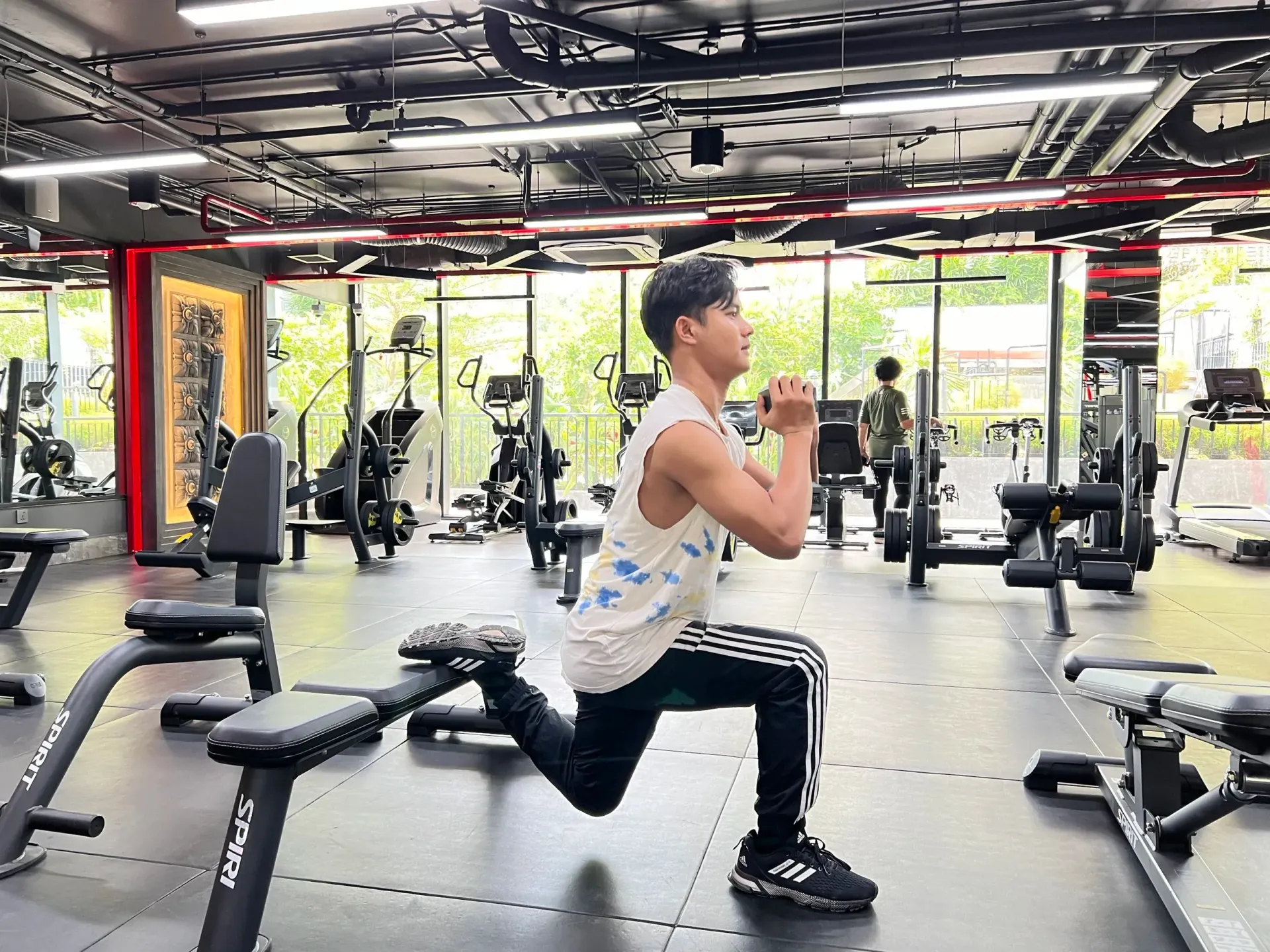 Man doing a dumbbell Bulgarian split squat in a gym.
