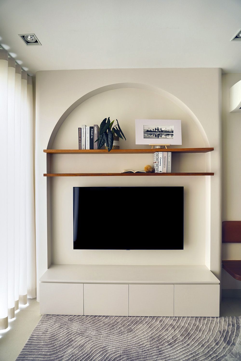 Wall-mounted TV in a beige alcove with shelves, decor, and cabinets in a modern living room