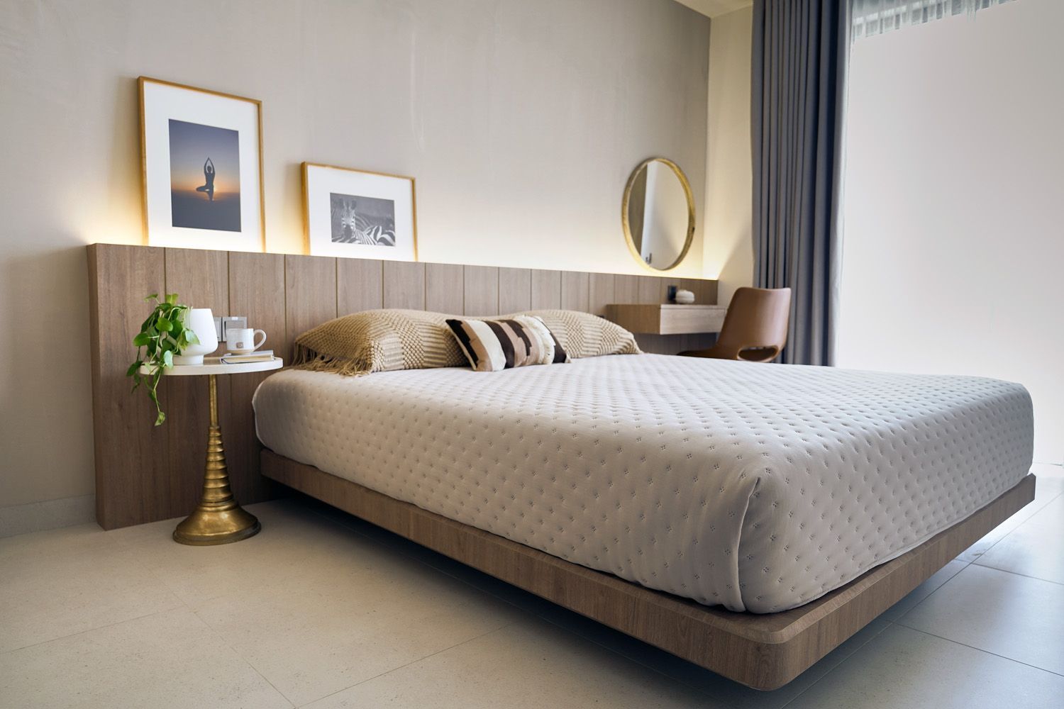 Modern bedroom with a large upholstered bed, bedside table, wall art, and natural light from curtains.