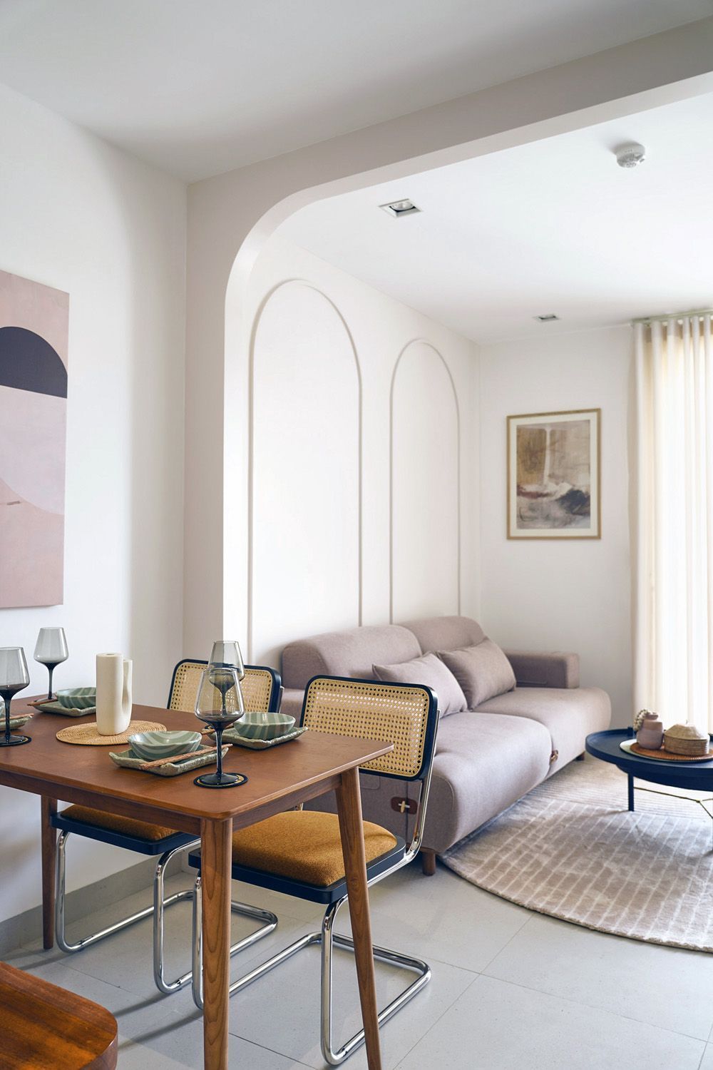 Bright living-dining room with a sofa, round rug, wooden table, and soft neutral decor