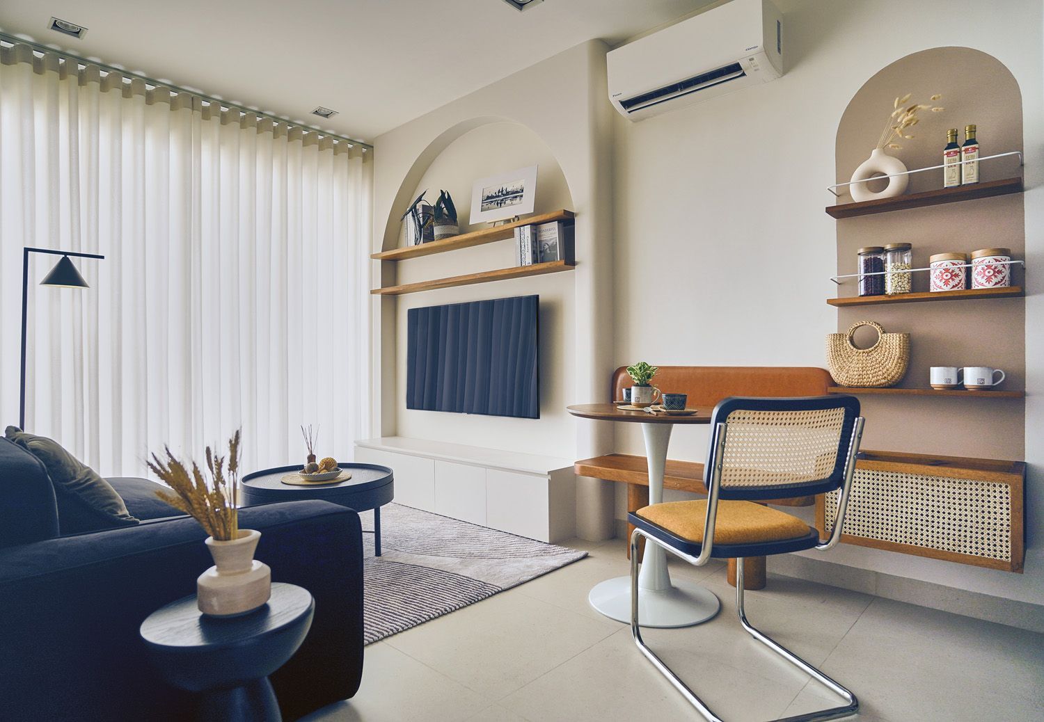 Modern living room with blue sofa, TV, arched wall shelf, desk, and large curtained window