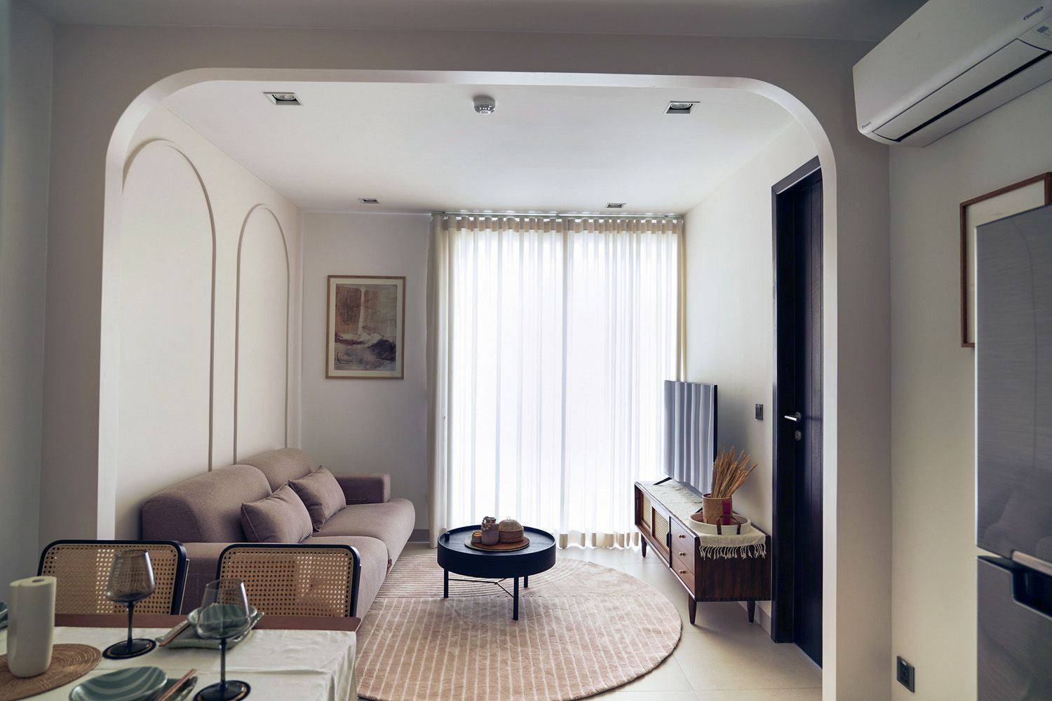 Modern living room with beige sofa, round rug, coffee table, and sheer curtains by bright window