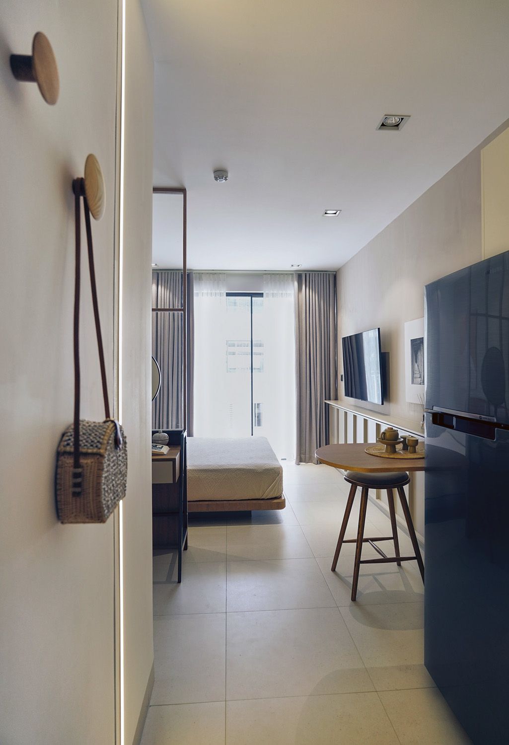 Modern bedroom with bed, desk, wall-mounted TV, and large window with curtains