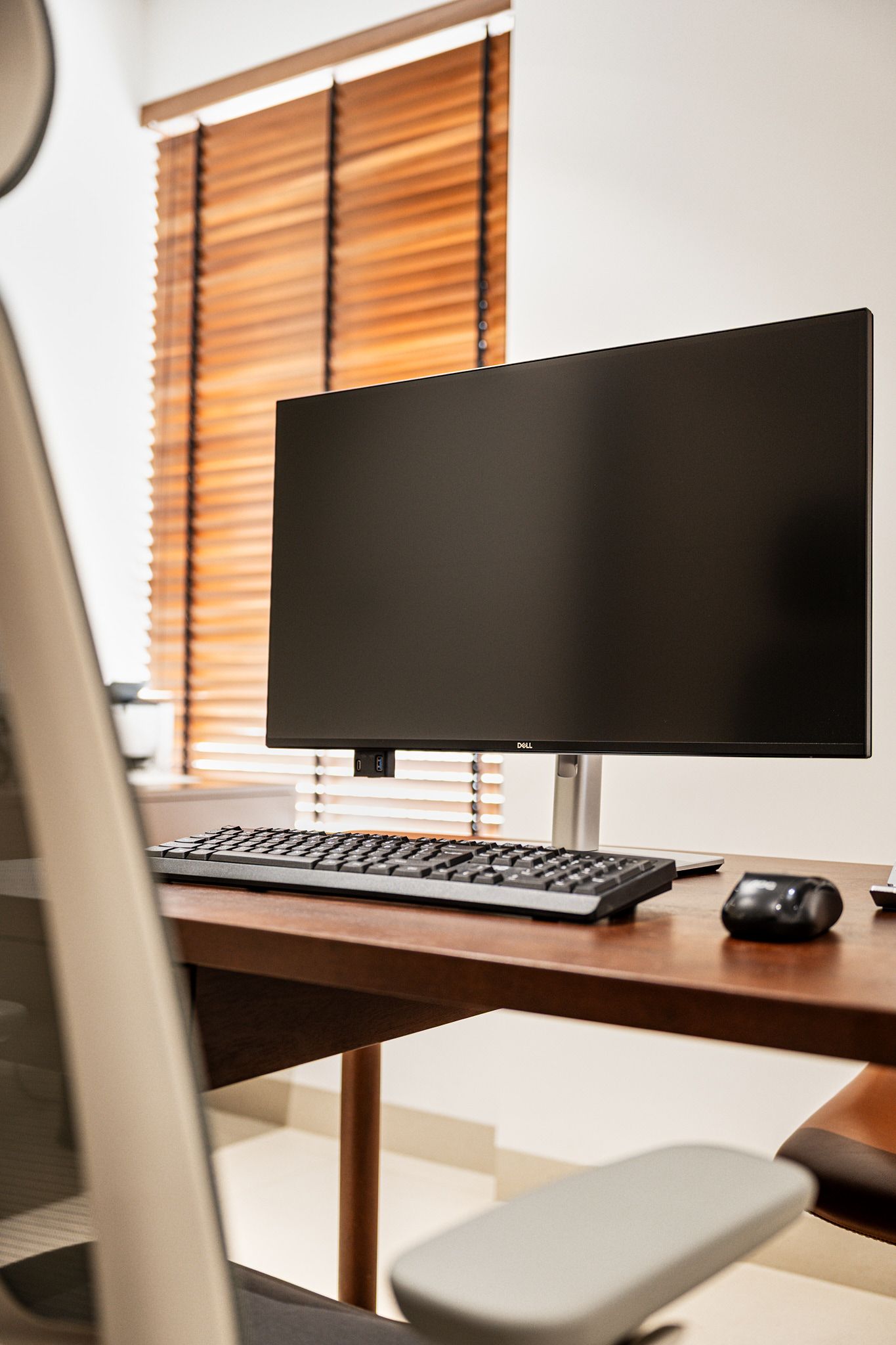 Modern desk setup with monitor, keyboard, mouse, and window blinds
