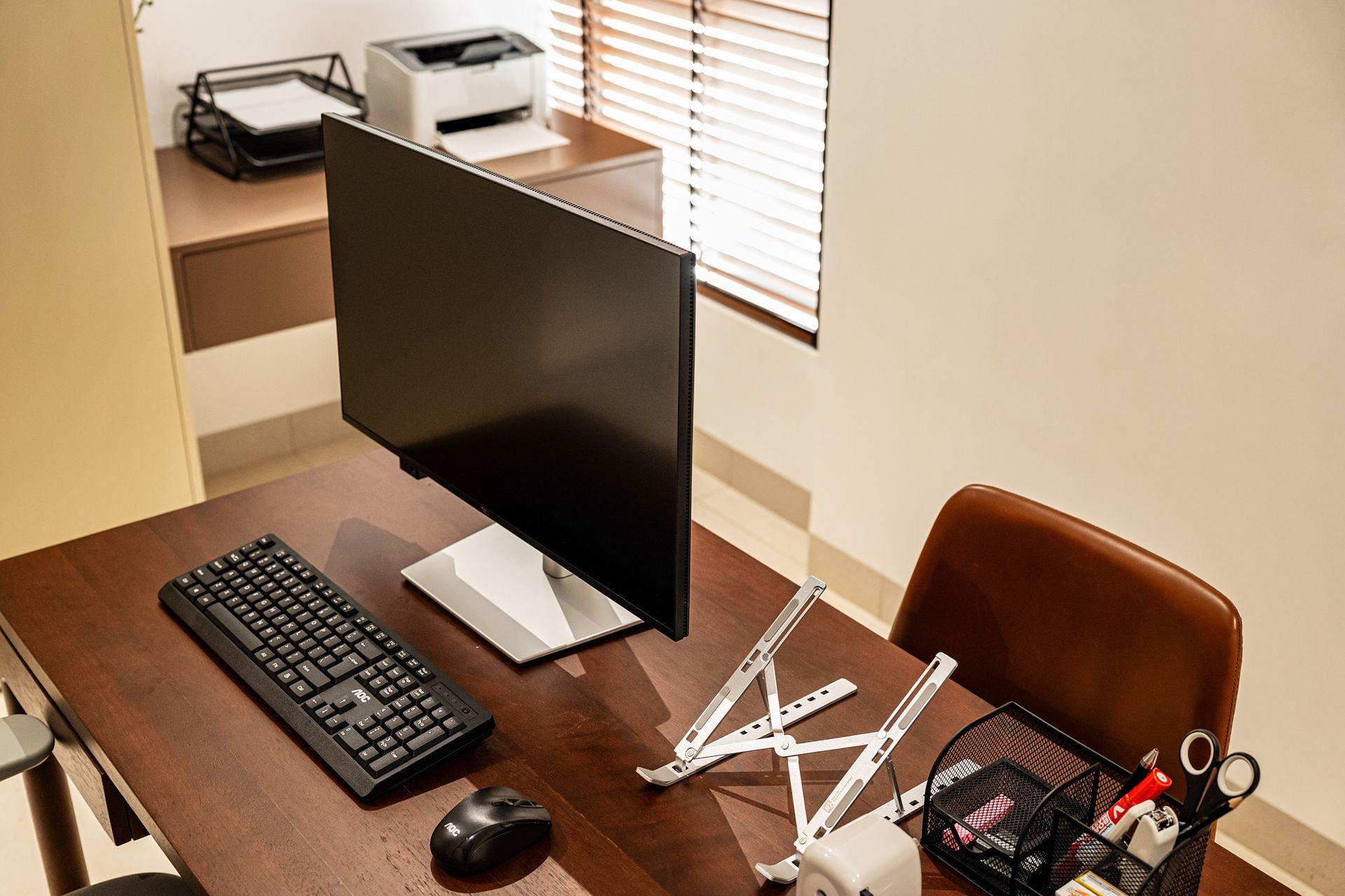 Desktop workspace with monitor, keyboard, mouse, printer, and office chair by a window