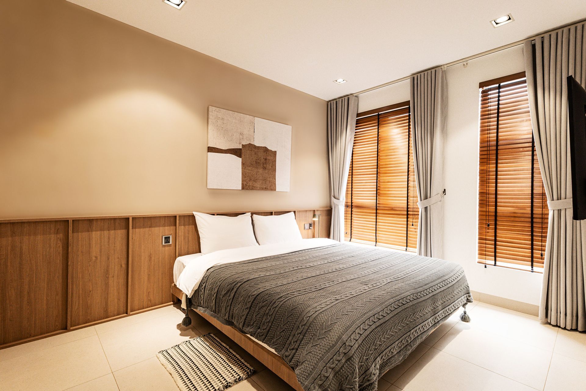 Modern bedroom with a bed, wooden cabinets, and large windows with blinds and curtains