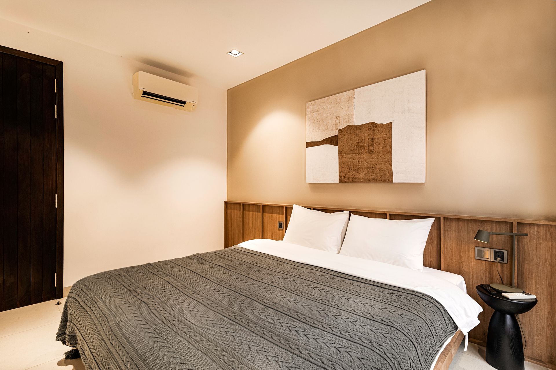 Modern bedroom with a king bed, beige walls, wood headboard, and abstract wall art