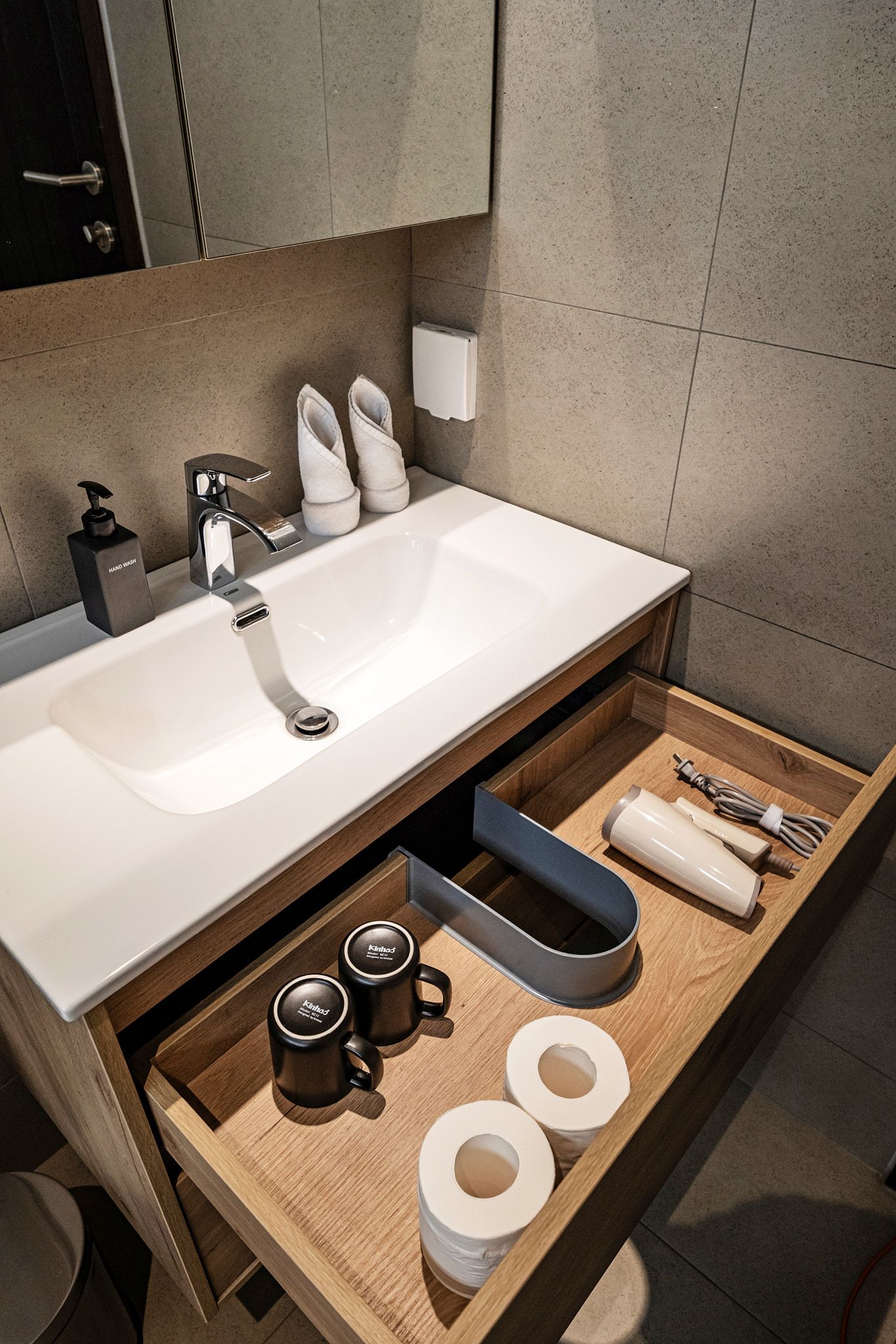 Modern bathroom vanity with sink, mirror, towels, and toiletries on a wooden drawer tray