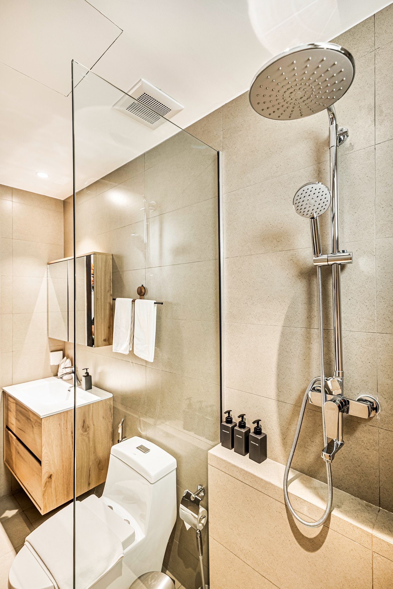 Modern bathroom with walk-in shower, beige tile, vanity, toilet, and round showerhead