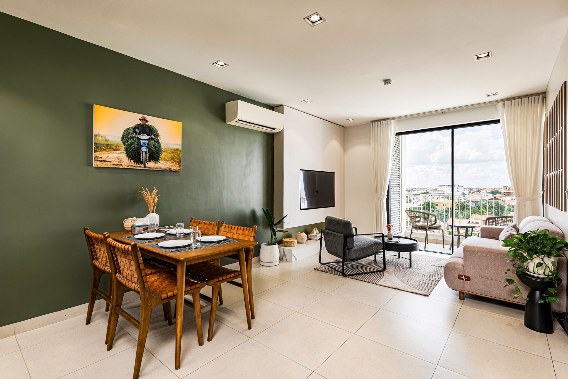 Bright living-dining room with green accent wall, wooden table, black chairs, sofa, and balcony view