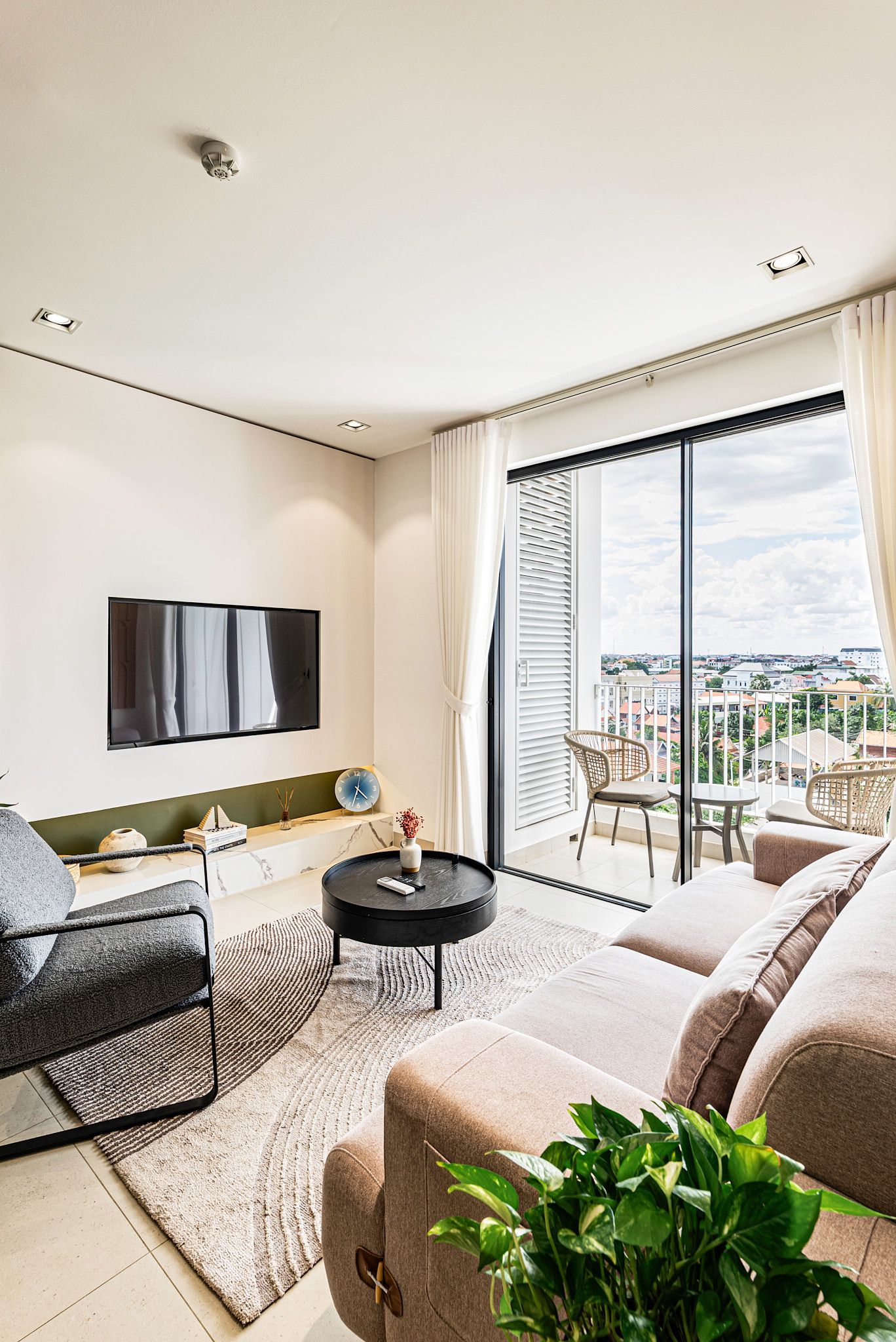 Bright modern living room with beige sofa, black coffee table, wall art, and sliding glass doors to a balcony.