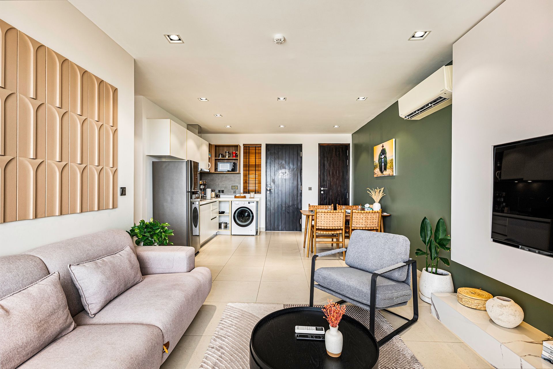 Bright modern living room with sofa, TV, green accent wall, and open kitchen area