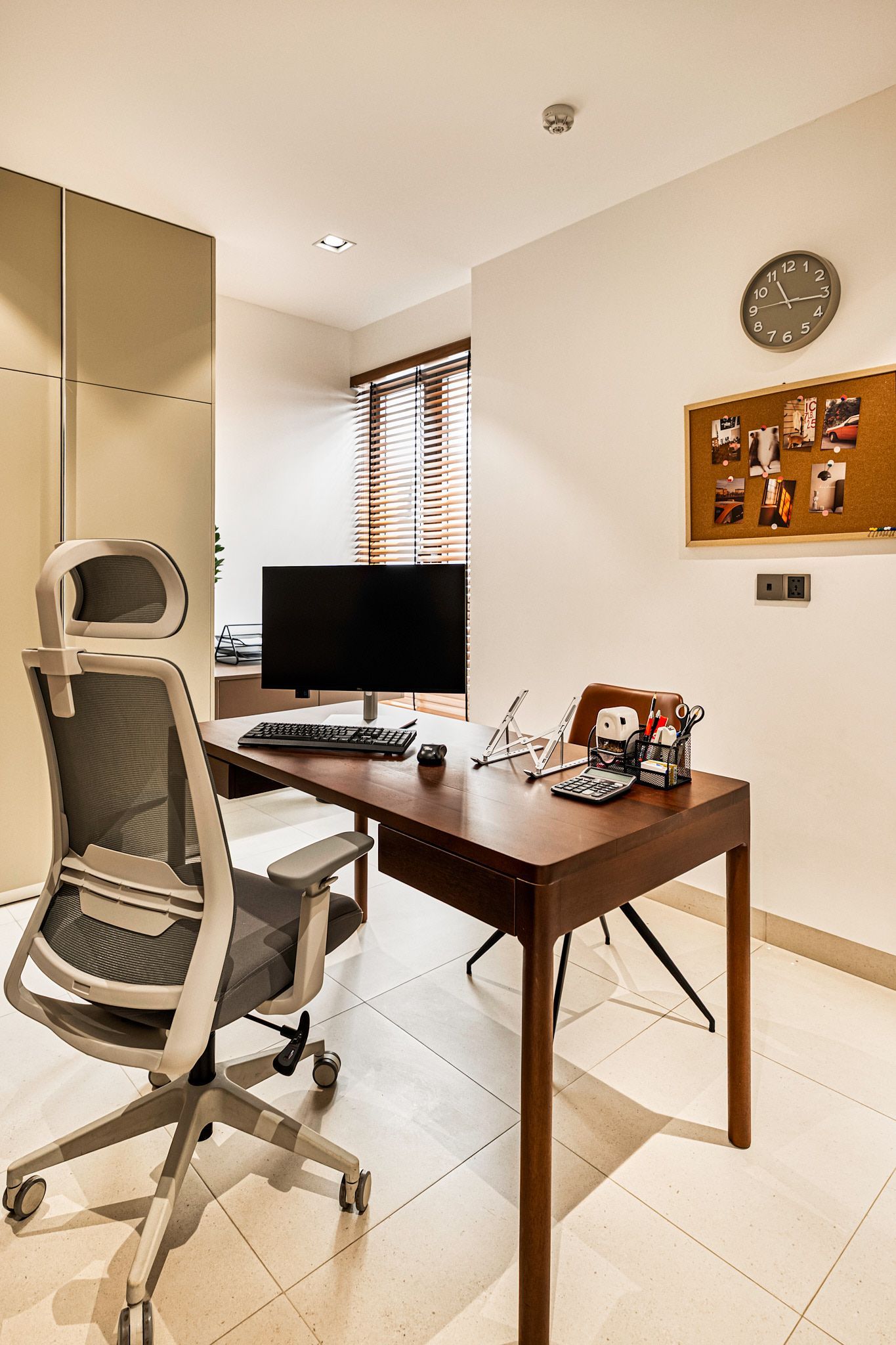 Small home office with a desk, computer monitor, swivel chair, wall clock, and corkboard.