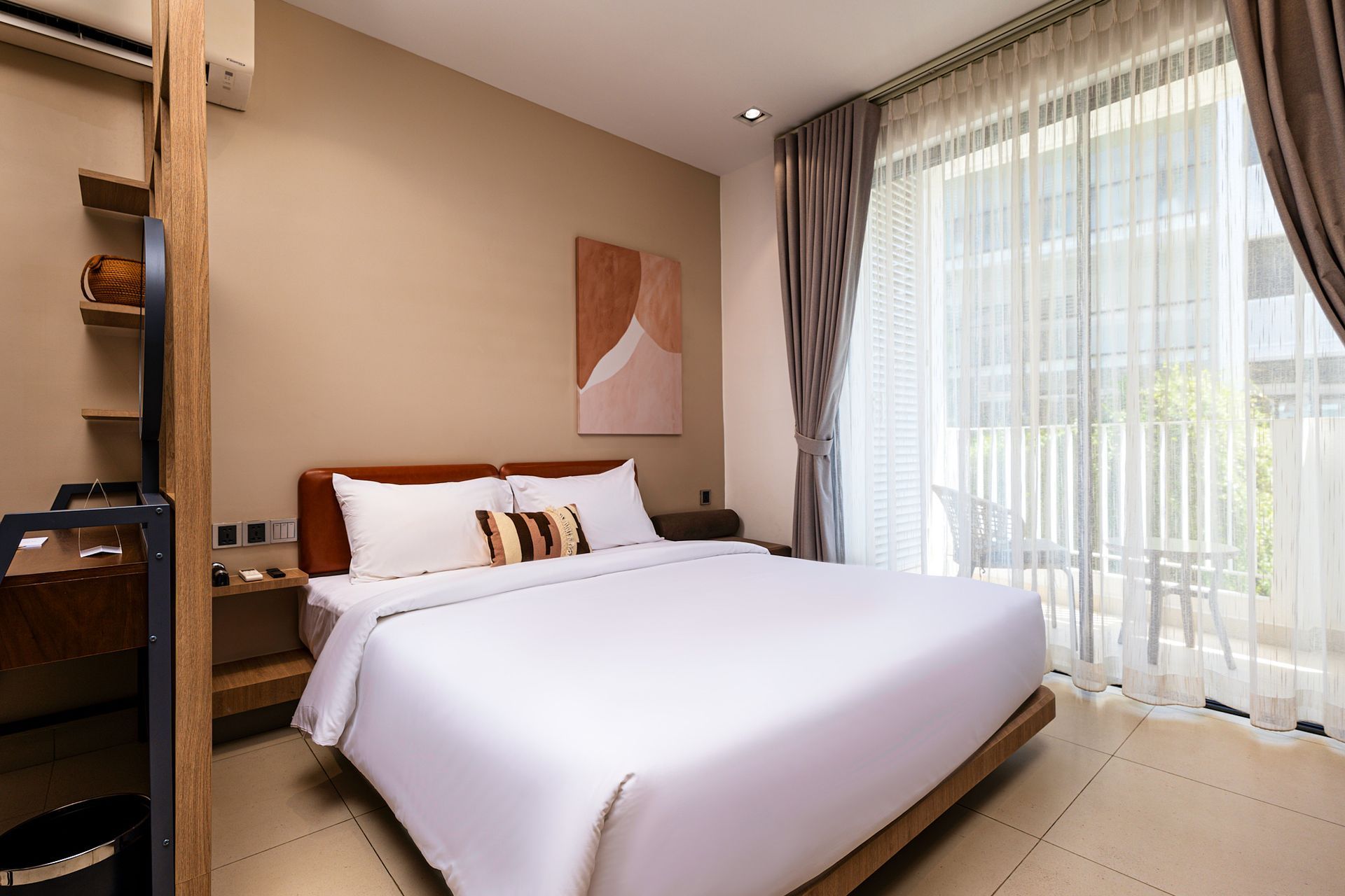 Modern bedroom with a neatly made white bed, warm wood shelving, and floor-to-ceiling sheer curtains