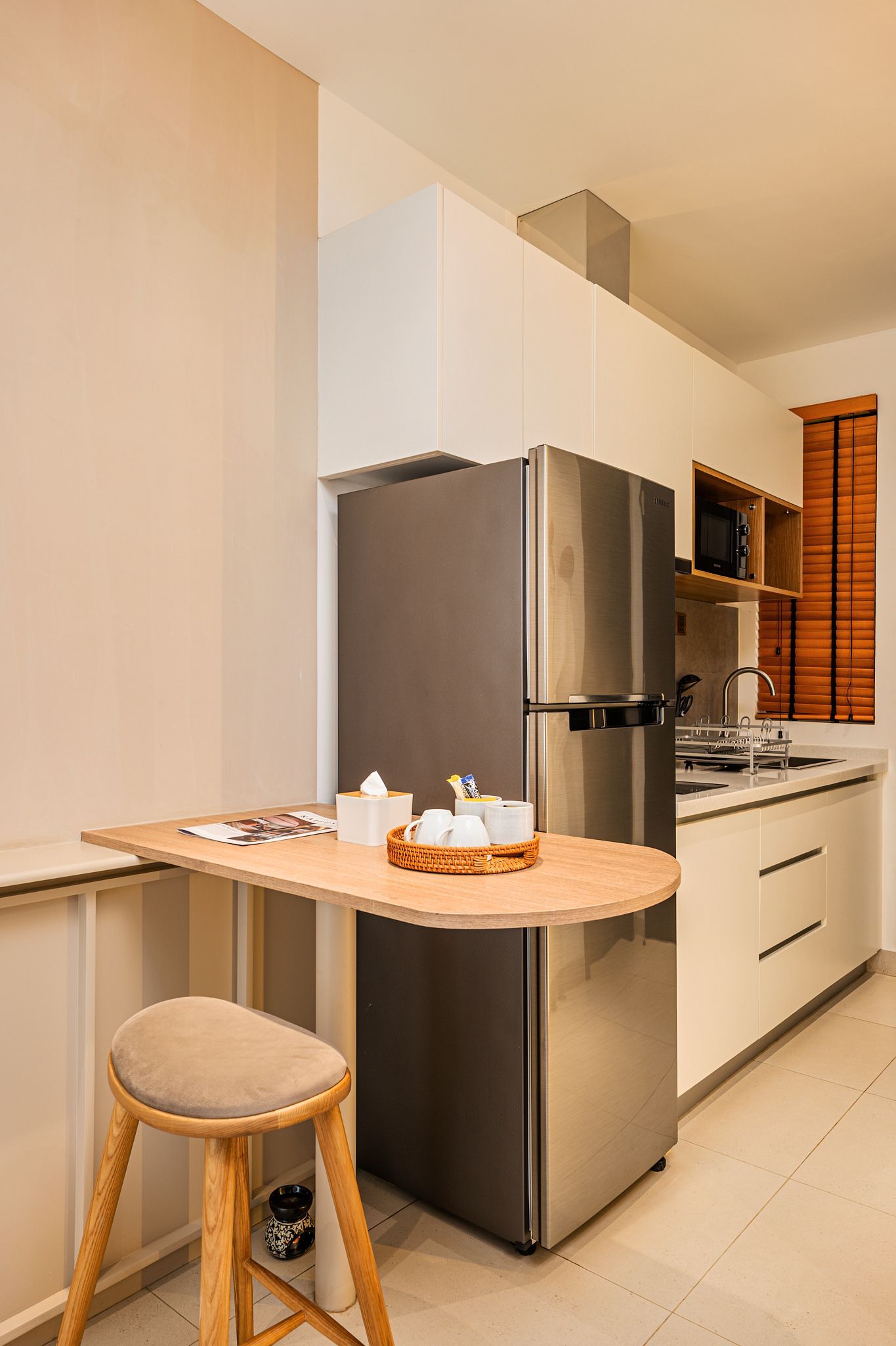 Compact kitchen with stainless steel fridge, white cabinets, and a small breakfast table with stools.