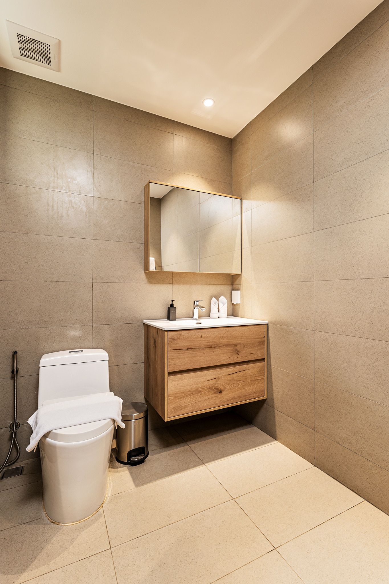 Small beige bathroom with toilet, wood vanity, mirror, and shower curtain.
